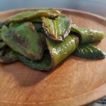 Roasted jalapeño peppers on a wooden plate with a charred, glossy appearance